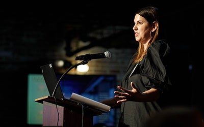 A woman in professional dress leads a discussion from a podium at the event.