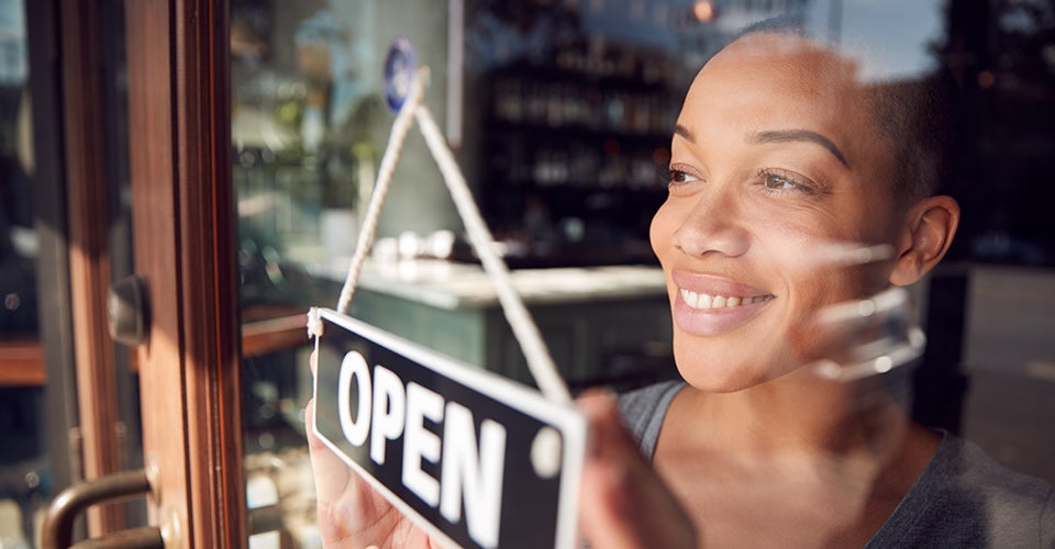 A woman flips the Open sign over on her restaurant as she looks out the window.