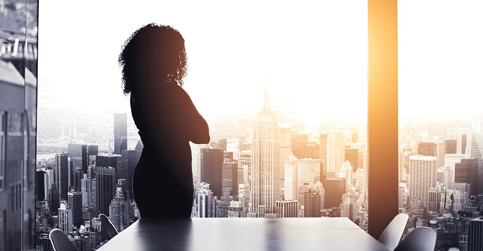 A young woman, silhouetted in a conference room, looks out onto the city skyline.