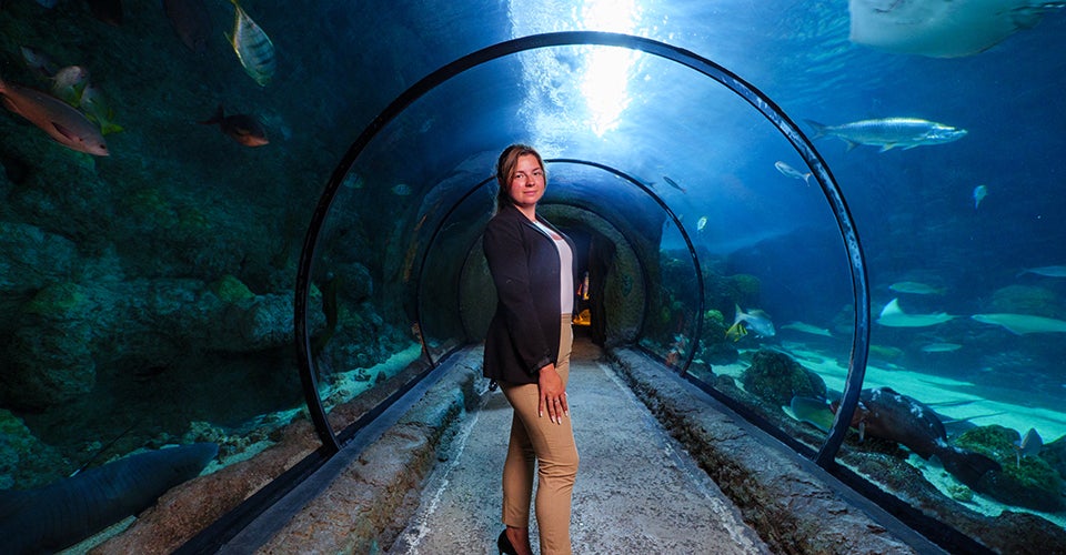 Emma Pearson stands in the Denver Aquarium as fish and rays swim by.