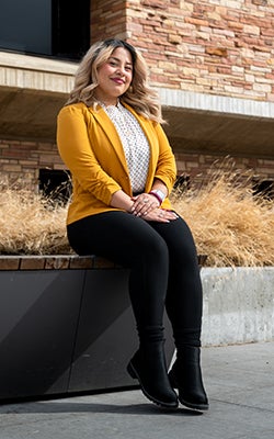 Jasmine in a gold blazer sitting outside the Rustandy Building.