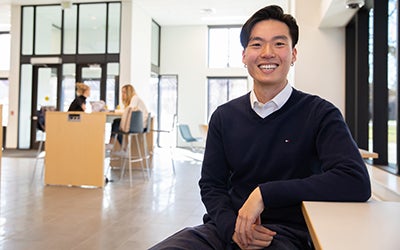 Will Xu smiles from a seat in the Rustandy Building.