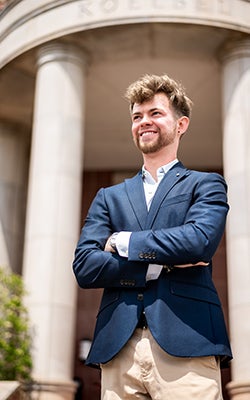 Matei in business casual attire, standing at the entrance of the Koelbel Building and looking off into the distance.