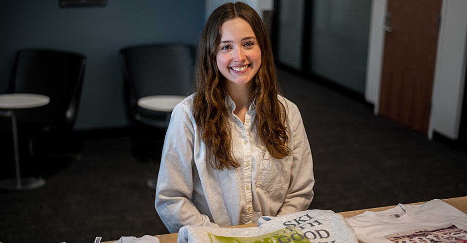 Holly at a table with some of her apparel, including hoodies and sweatpants.