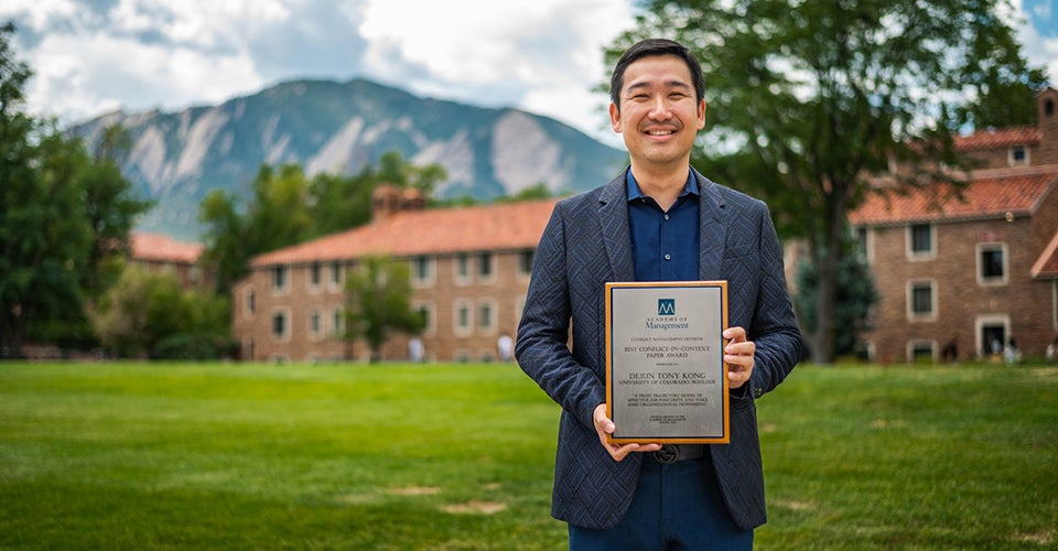 Tony Kong poses on the quad with his award. The mountains are visible in the background.