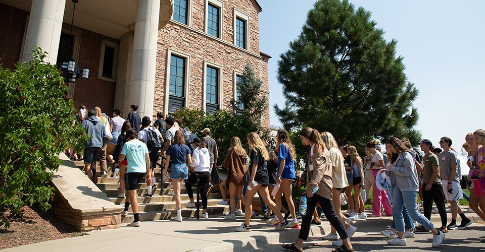 A group of first-year students walking into the Koelbel Building on a sunny day.