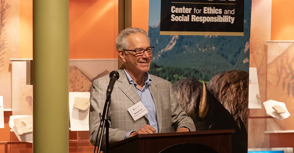 Michael Leeds speaking at a podium in a museum.