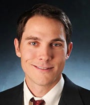 Headshot of Brian Lewandowski in a dark suit against a blue background.