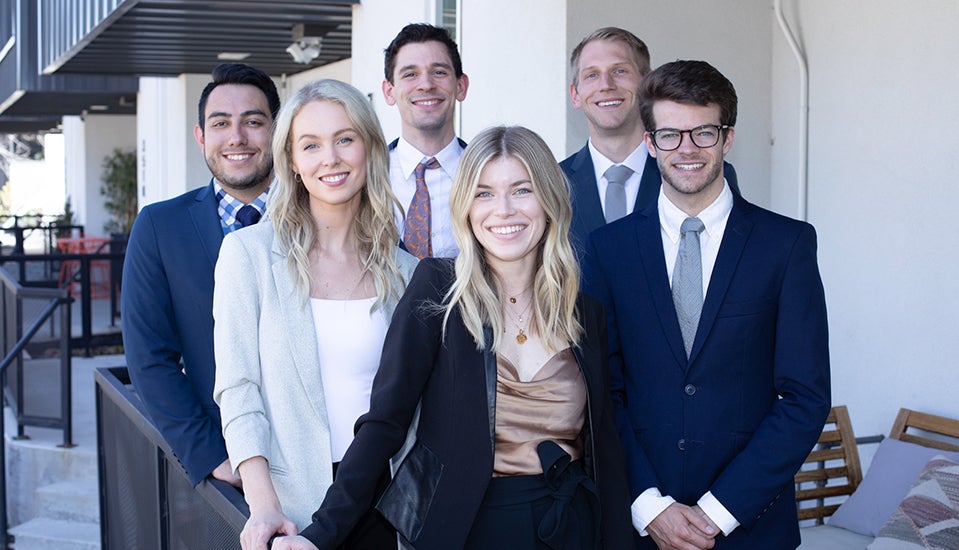 Four male and two female students pose as a group in professional dress.