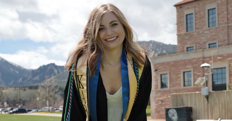 Olivia posing in in graduation regalia outside the Koelbel Building.