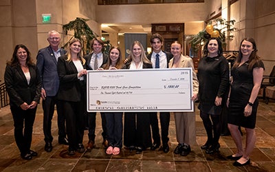 The students, along with Omni representatives, pose with a giant check in the hotel's lobby.
