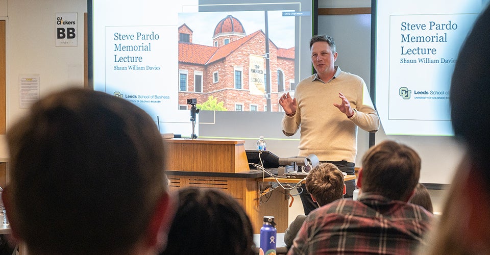 Shaun Davies presenting at the podium. Students watching the talk can be seen in the foreground.