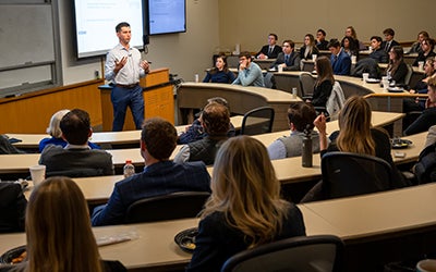 A crowded lecture hall seen from the back. Brian Waters is speaking in front of the classroom.