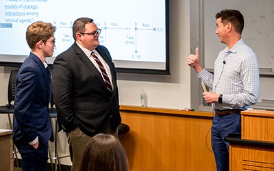 Three men in professional attire in front of a lecture hall.