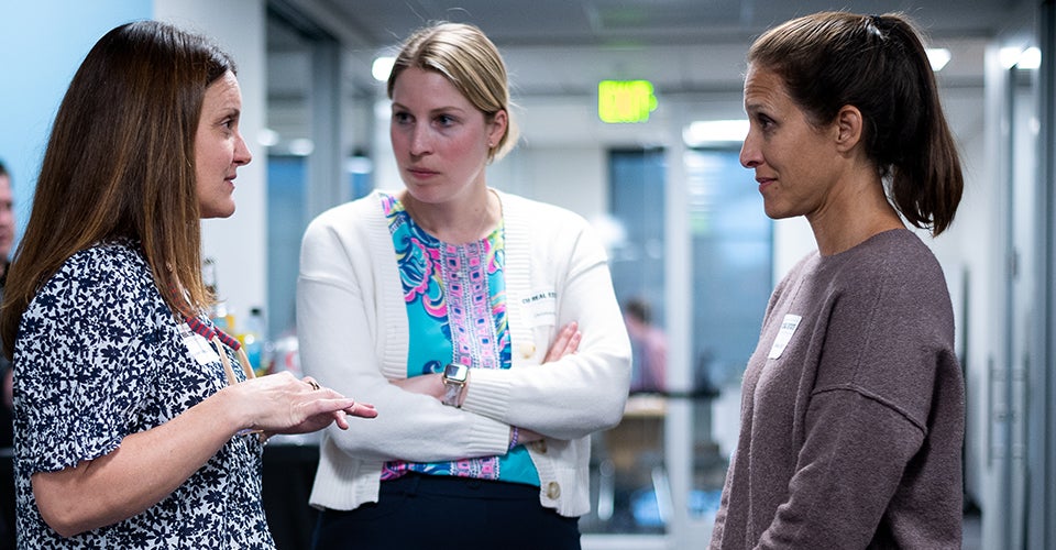 Three female professionals in business attire chat in a corridor in the Koelbel Building.