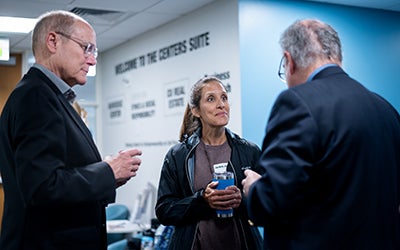 A female student speaks with two male faculty members.