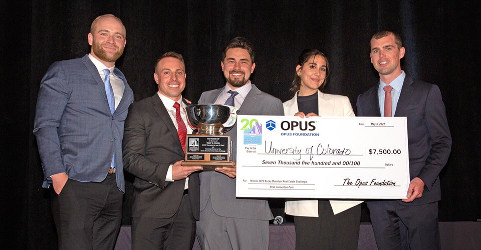 Five students in professional dress stand with a lovely check and trophy.