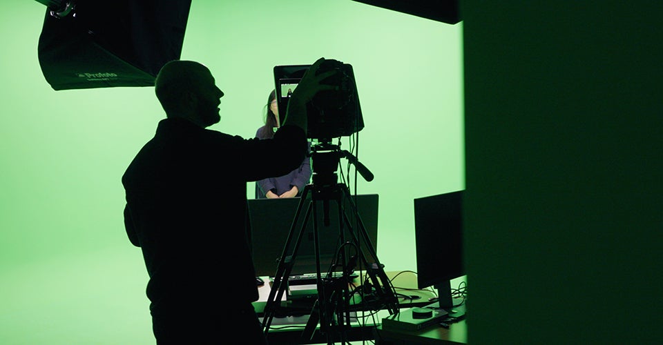 Silhouette of people against a green screen. Recording equipment is visible in the foreground.