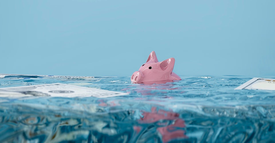 A piggy bank is mostly underwater in a pool. Also floating is U.S. paper currency.