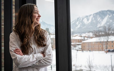 Holly looks out a window onto a winter scene, with mountains in the background.