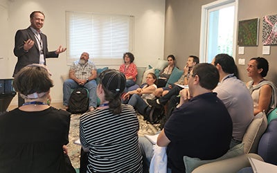 A male professor leads a group discussion in a crowded room.