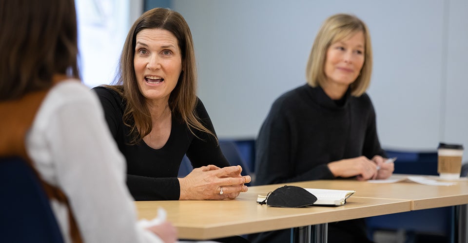 Two women in professional dress address a panel in a lecture hall.