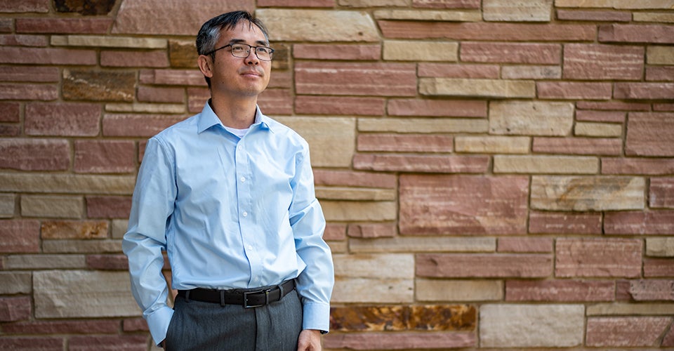 Dan Zhang dans une pose détendue près d'un mur de briques.