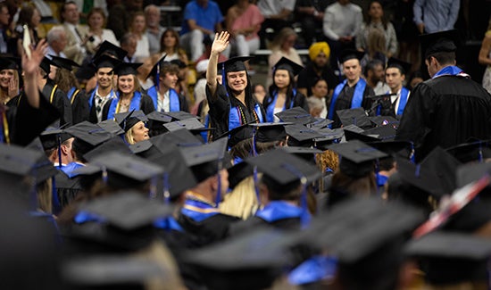 A woman waves to her family during commencement. She's surrounded by other graduates.