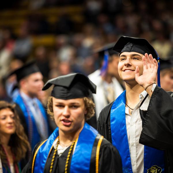 A graduate waves at family in the audience