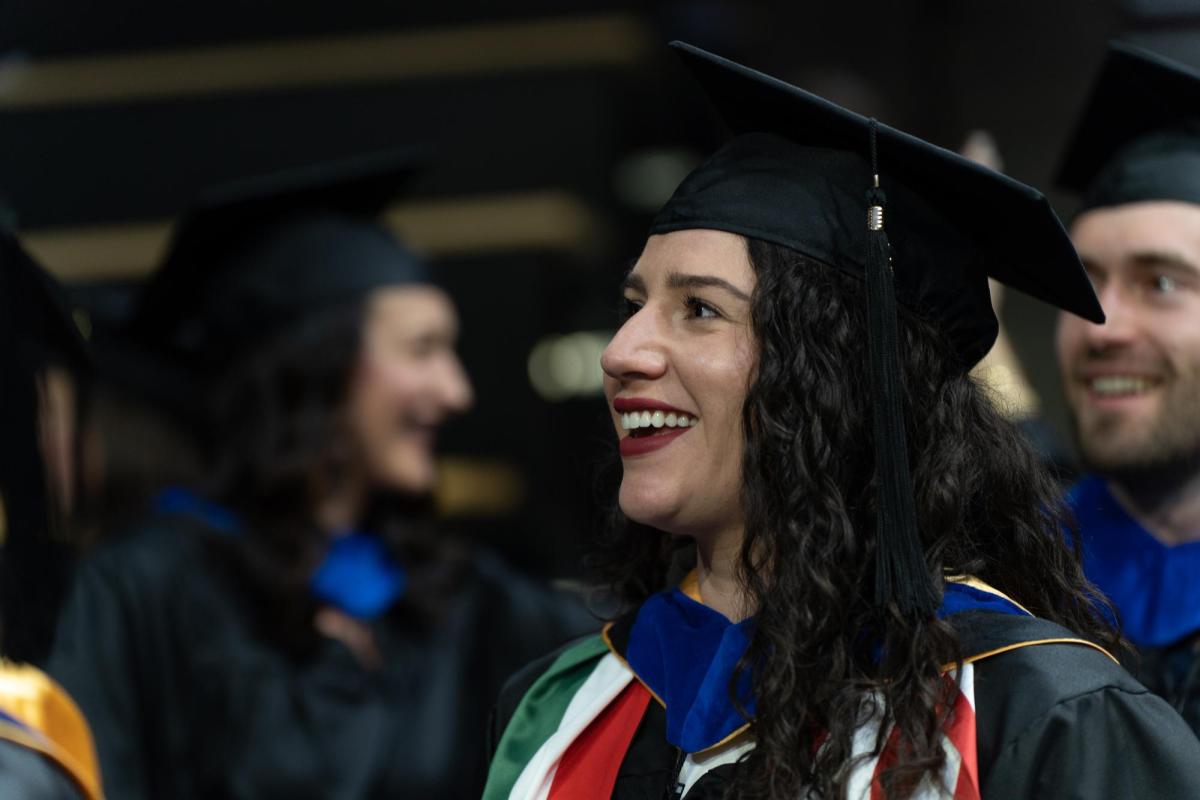 Student wearing graduation regalia smiles while looking out of frame.