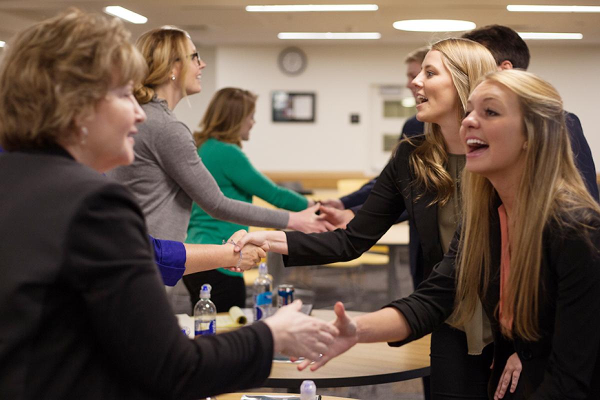A group of female students and professionals shake hands at a recruiter event.