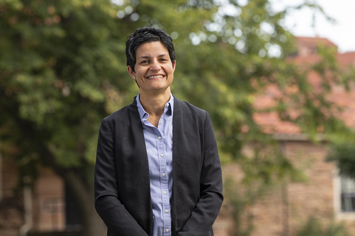 Yonca in professional dress outside the Koelbel Building, which is visible in the background.