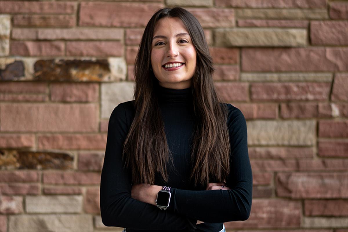Kyla stands against a sandstone brick wall.