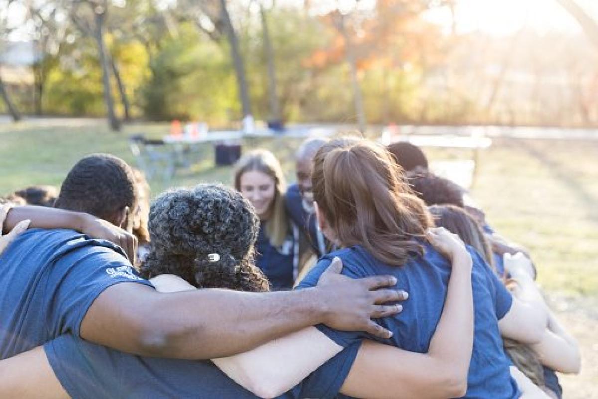 group hugging outside under some trees with their backs turned
