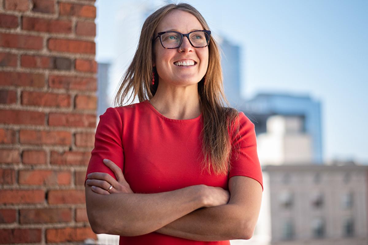 A professional woman in a red dress poses confidently on a rooftop.