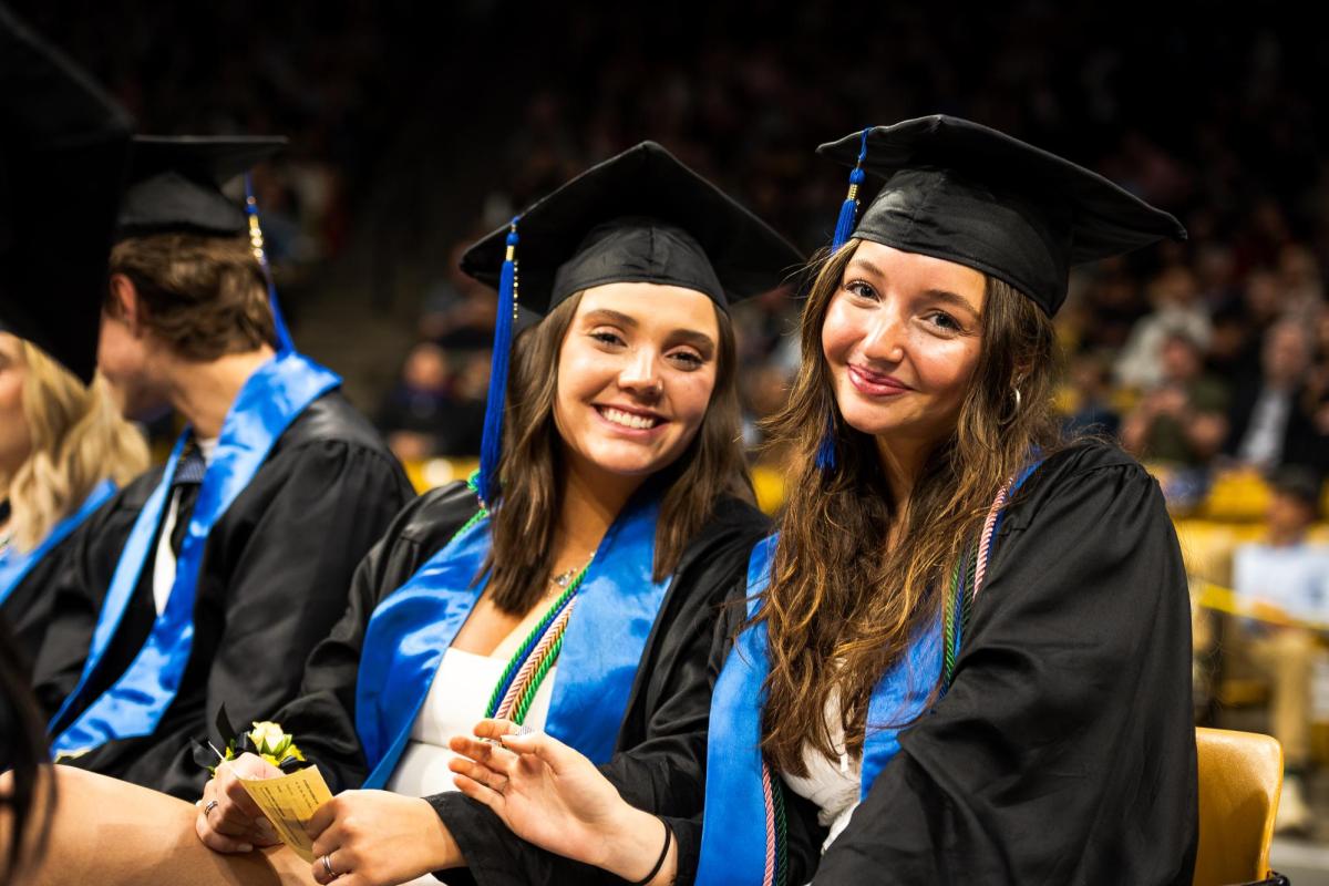 Two graduates in regalia smile at the camera during the ceremony.
