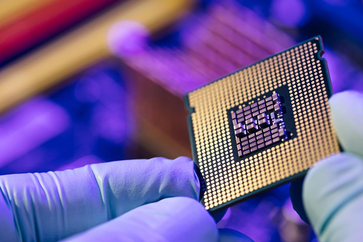 A worker in gloves holds a semiconductor chip.