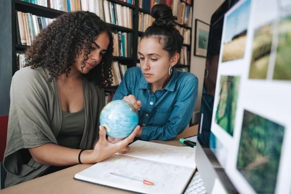 Two women holding a globe and collaborating in front of a computer