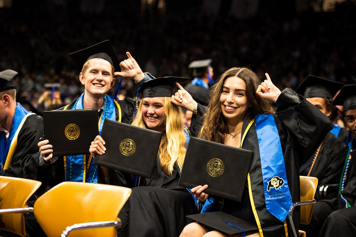 Graduates smile for the camera while holding up their diplomas.
