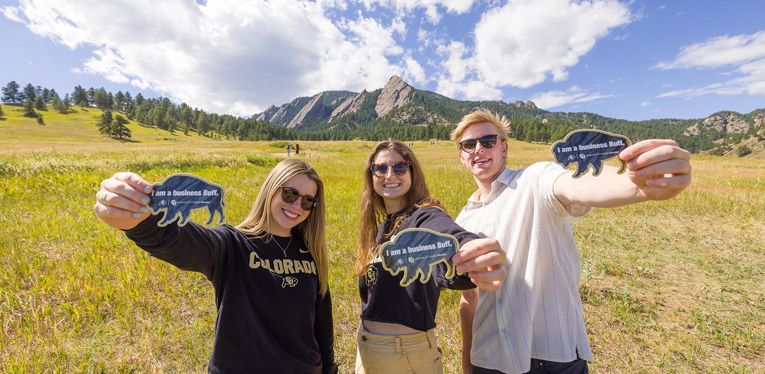 Leeds ambassadors hold up #BusinessBuff stickers while smiling in front of the Flatirons