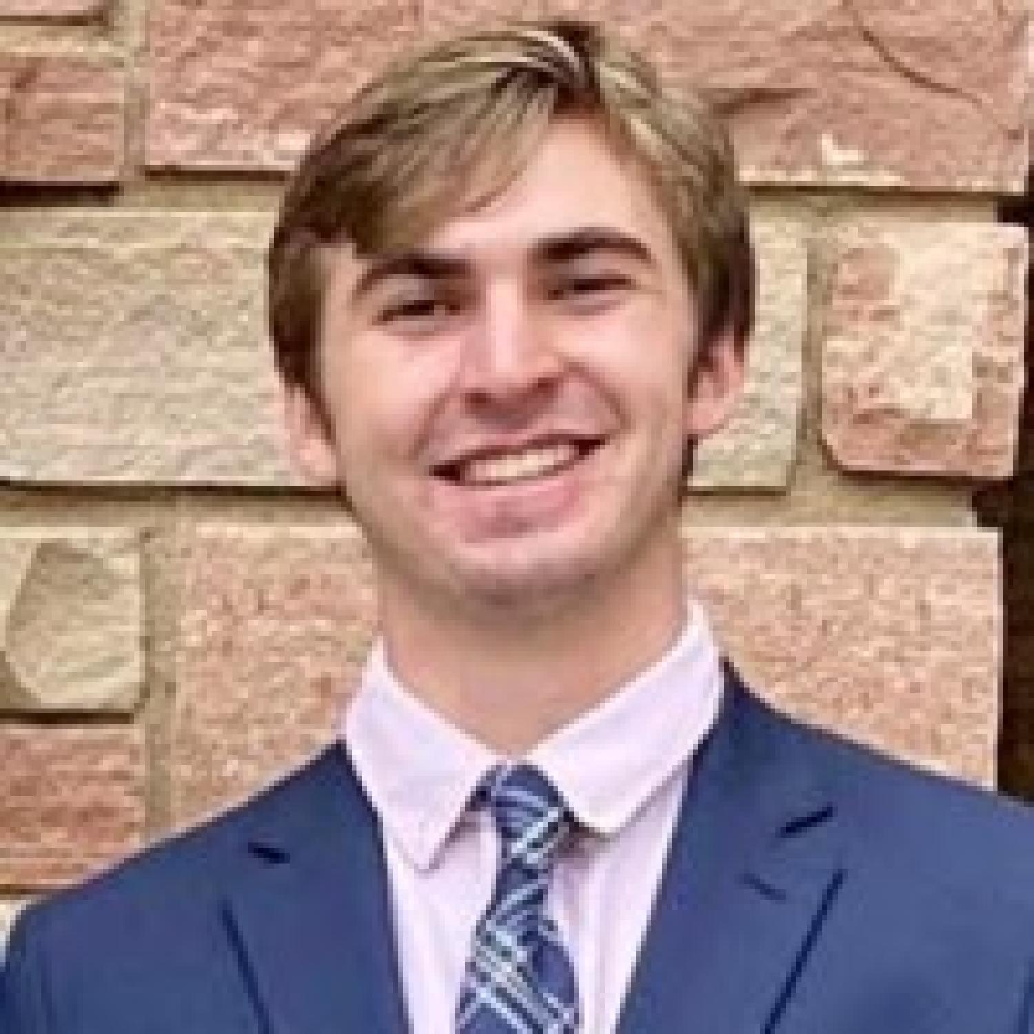 Sean Boselli in a suit smiling pictured against brick