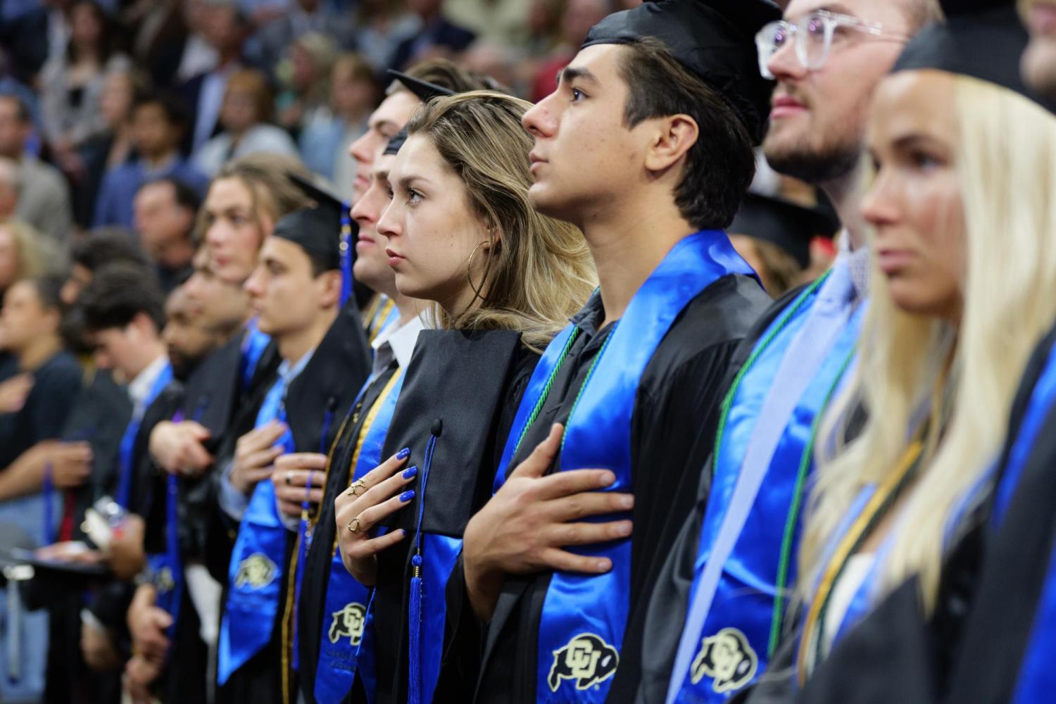 Students in regalia place their hands over their hearts during the national anthem.