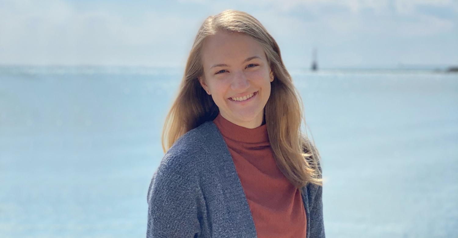 Claire McCollough stands on a beach. The ocean is visible in the background.