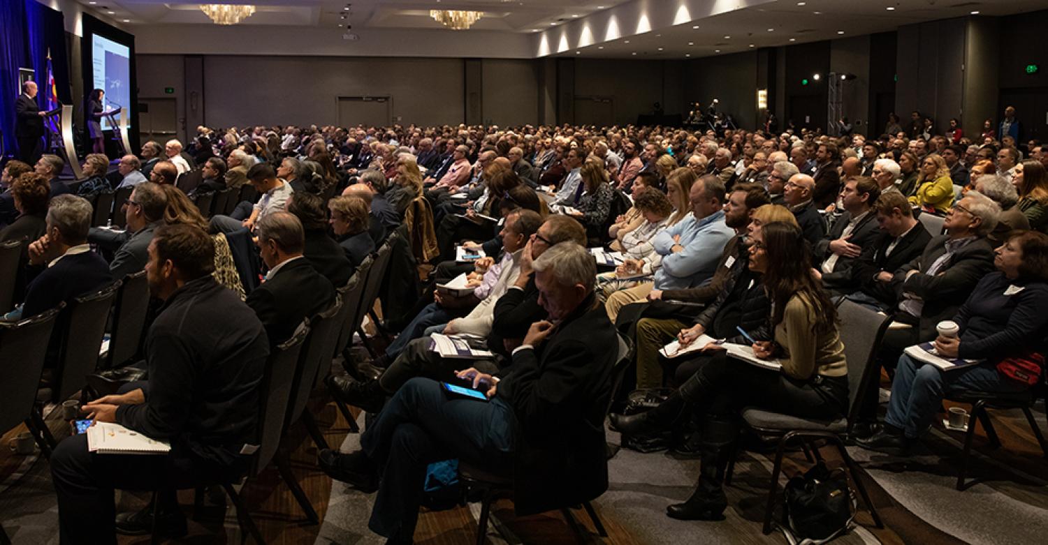 Crowd shot from the Business Economic Forum. Hundreds of professionals are gathered in a ballroom.