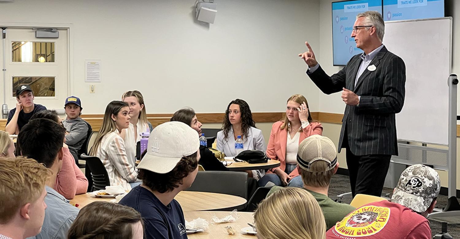 Clark Jones, in a suit, makes a point in the front of a crowded classroom. Other students look back to see the student Clark is talking to.