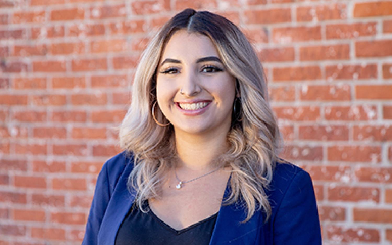 Nataly in professional dress against a brick wall.