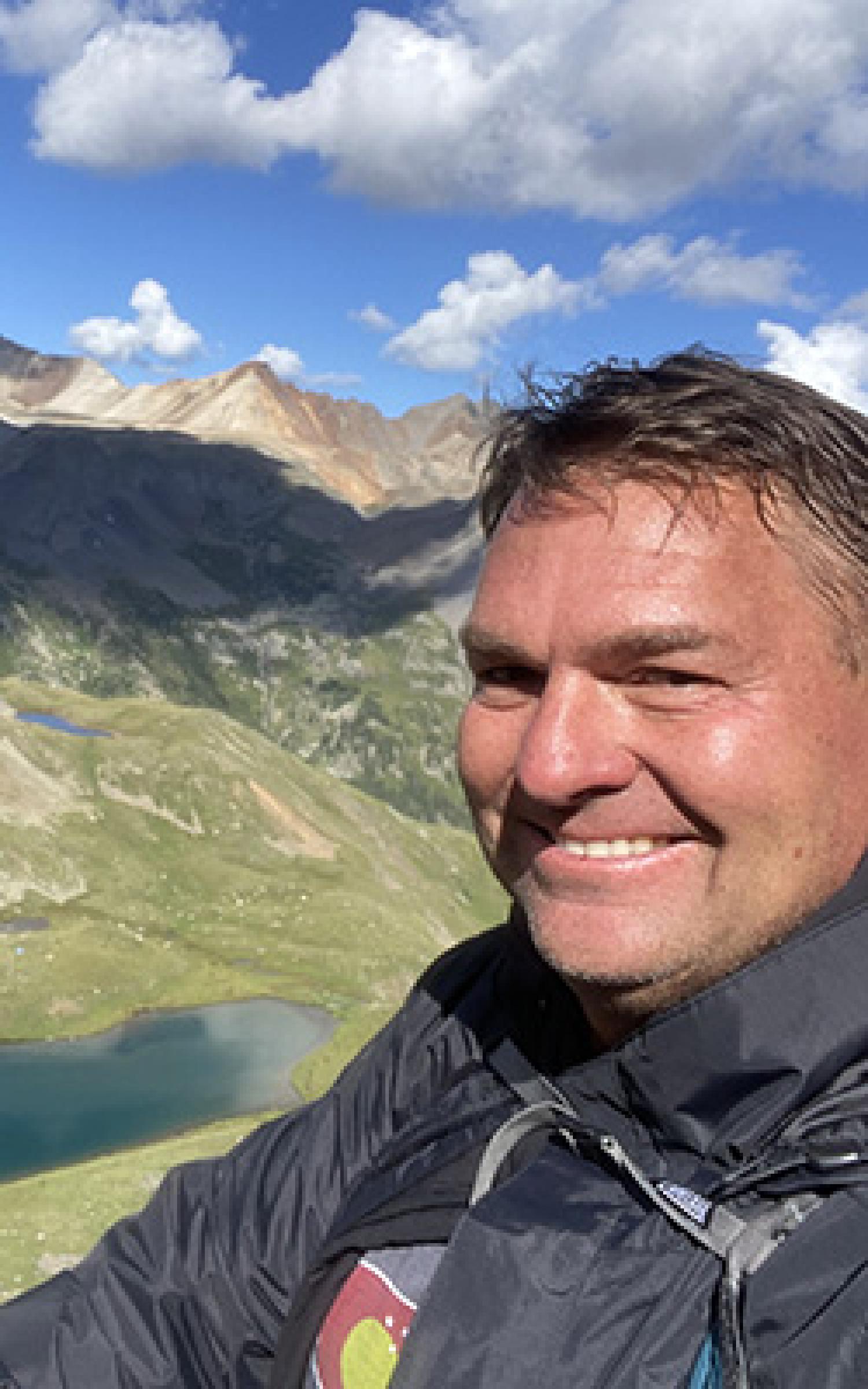John Quinn on a hiking trail. Mountains are visible in the back.