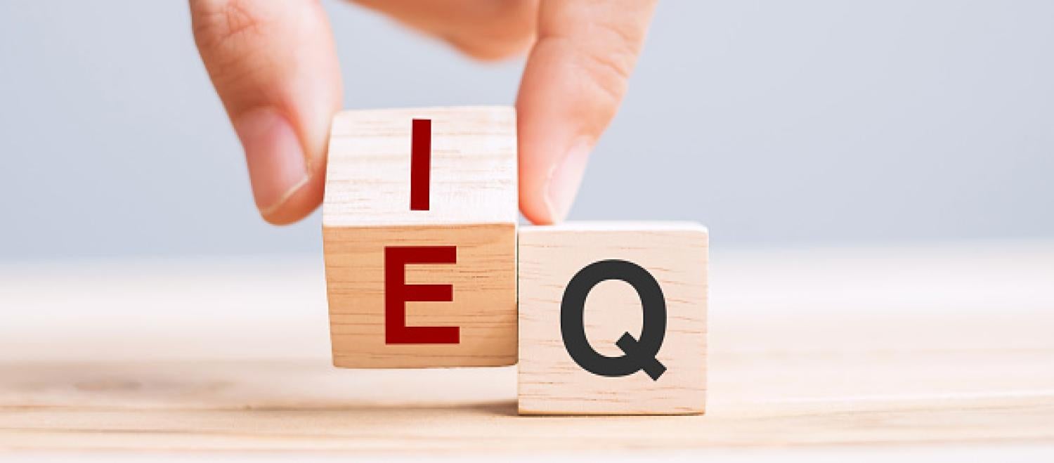 A hand turns a wooden blocks from "E" to "I", while a stationary block shows the letter "Q"