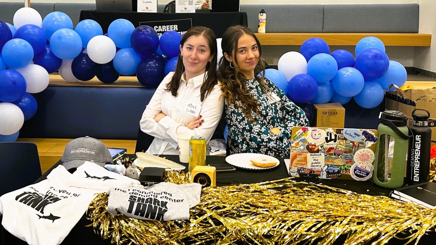 Mackenzie Culver and Rhiannon Martin posing with their backs together at a table.