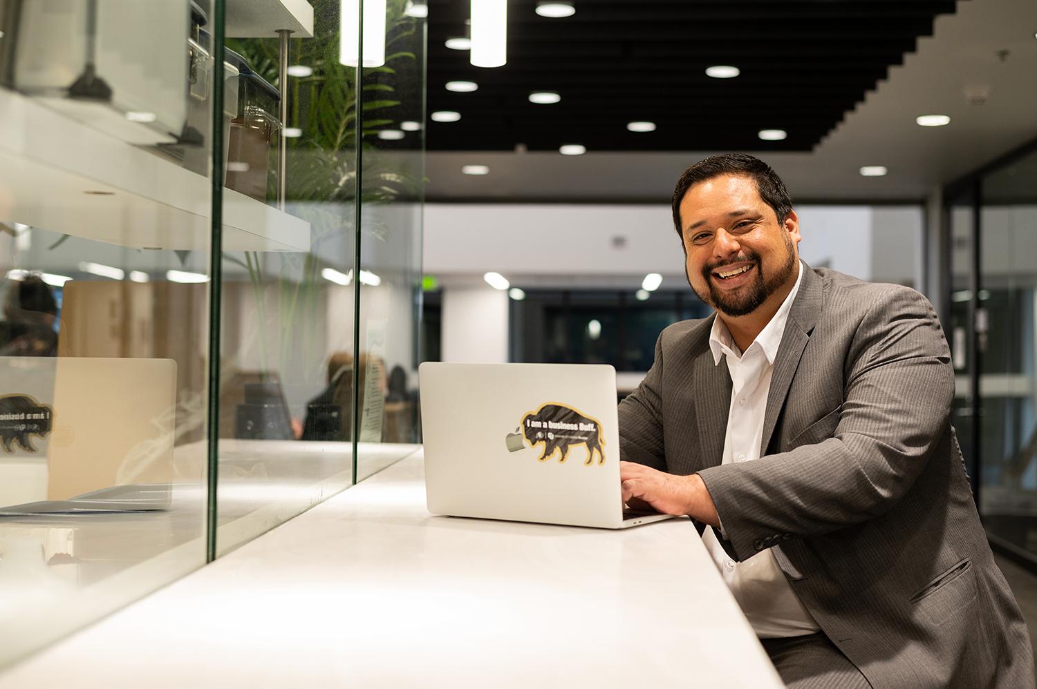 Joe Constancia smiles while working on a laptop at a counter